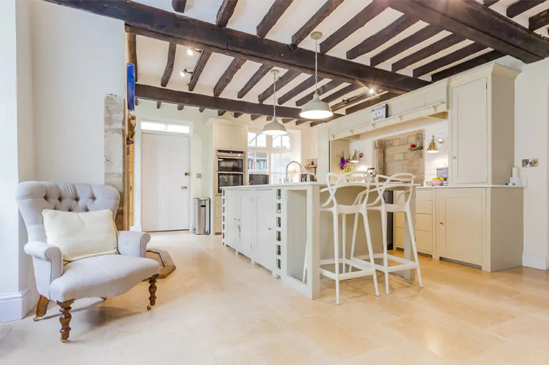 Bright country kitchen with wooden beams across the ceiling and stone flooring throughout.