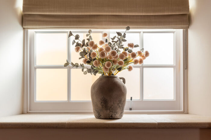 A stone windowsill with a vase as the centrepiece with an arrangement of dried flowers.