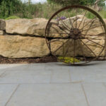 Wagon wheel resting against a stone wall on paving stones