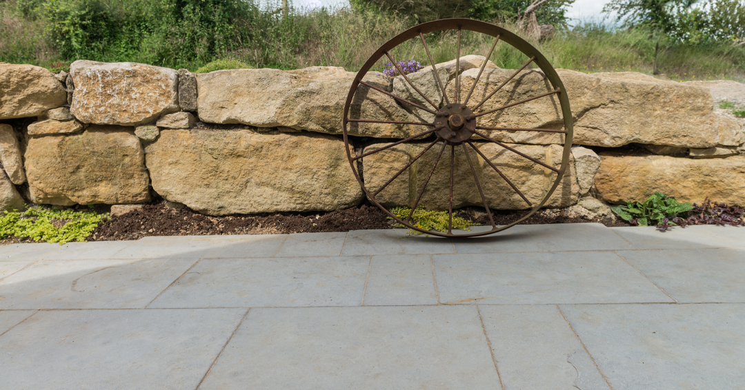 Wagon wheel resting against a stone wall on paving stones
